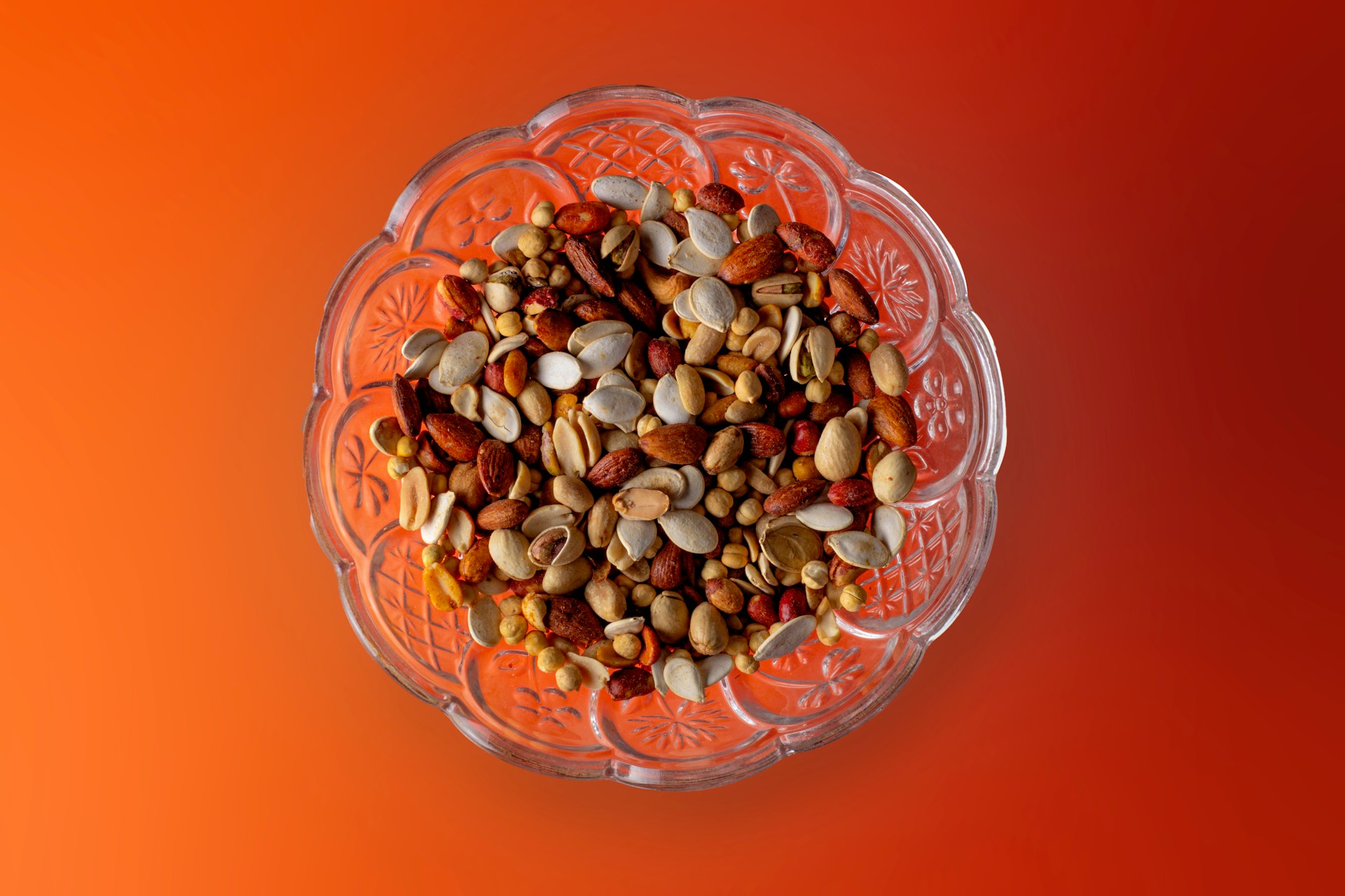 description: Overhead shot: A bowl of mixed nuts, on an orange backdrop.  Photo by Usman Yousaf on Unsplash.