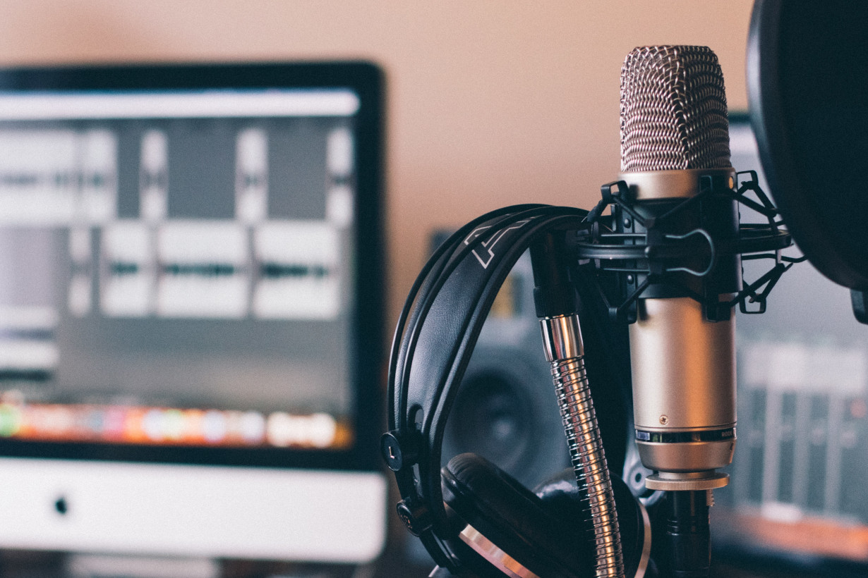 Description: Image of a microphone (in focus), with a computer screen in the background (blurry).  Photo by Will Francis on Unsplash.