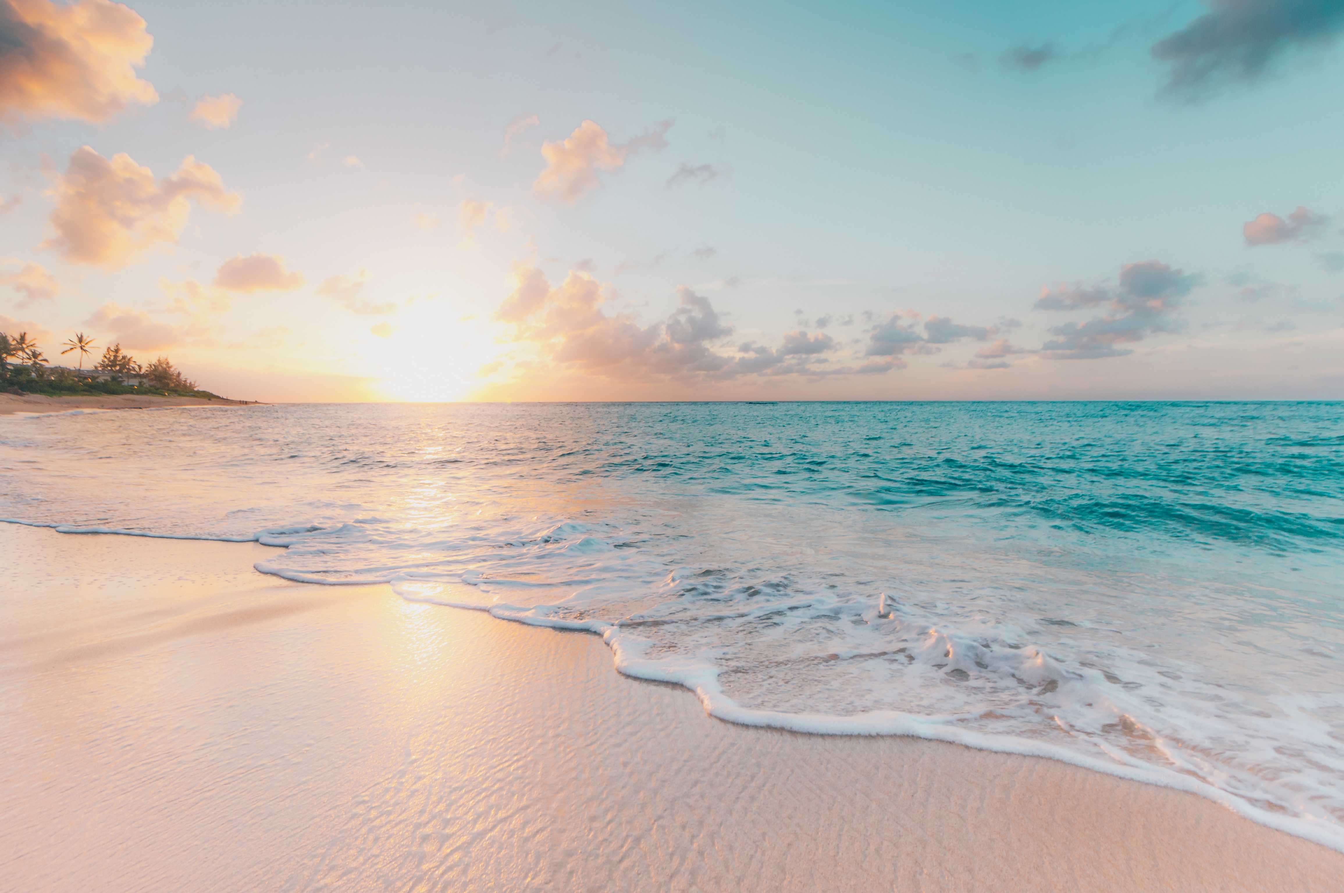 A photo of a sunset on the beach in Oahu, Hawaii.  There is pale, clean sand in the foreground and blue water in the background.  Photo by Sean Oulashin on Unsplash.