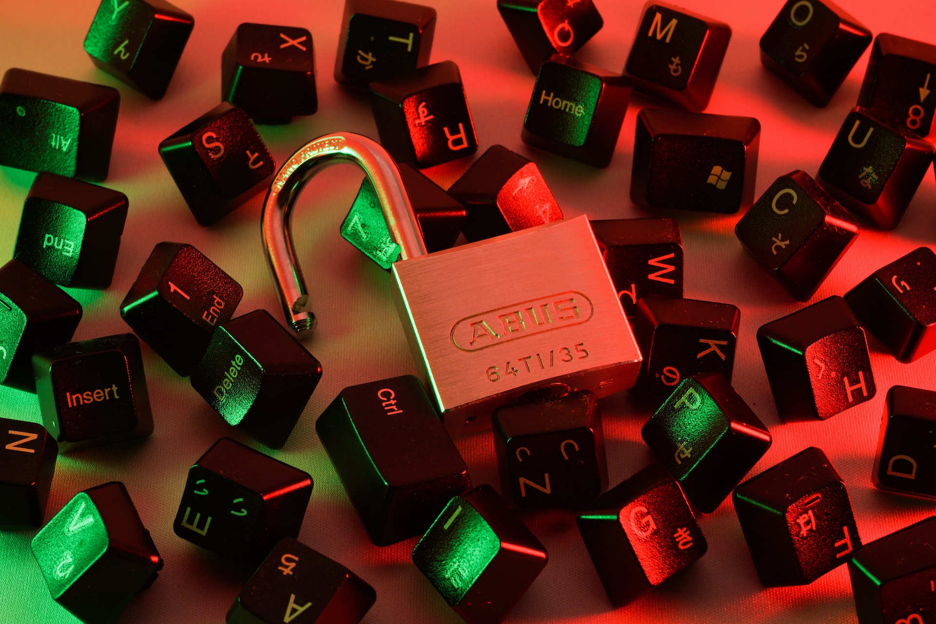 An image of an open padlock, surrounded by computer keyboard keys.  The scene is cast in a reddish light. Photo by FLY:D on Unsplash
