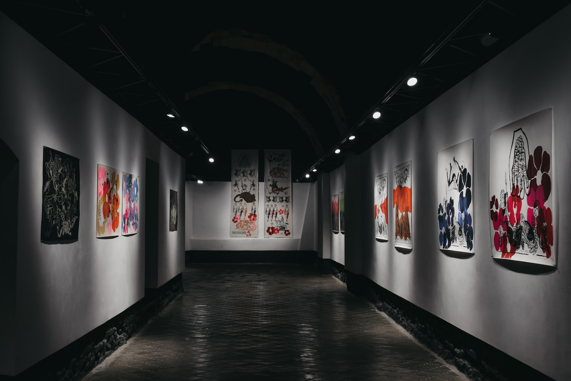 description: An image of a hallway in an art gallery.  Colorful paintings hang on the walls to the left and right, and also on the wall ahead.  Photo by Darya Tryfanava on Unsplash.