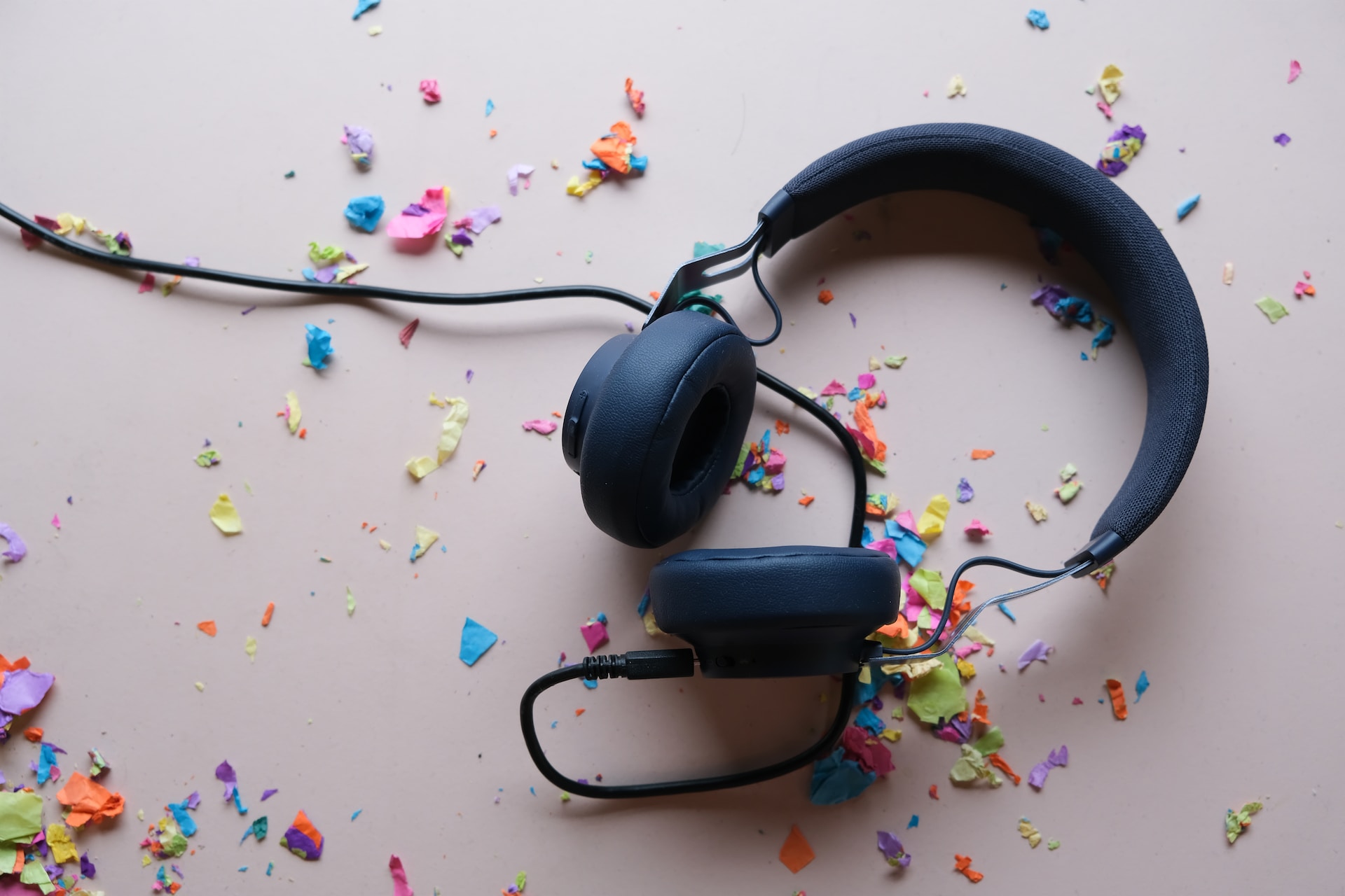 description: Description: A set of black, wired, over-the-ear headphones on a table.  There is colorful confetti scattered about.  Photo by Ryan Quintal on Unsplash.